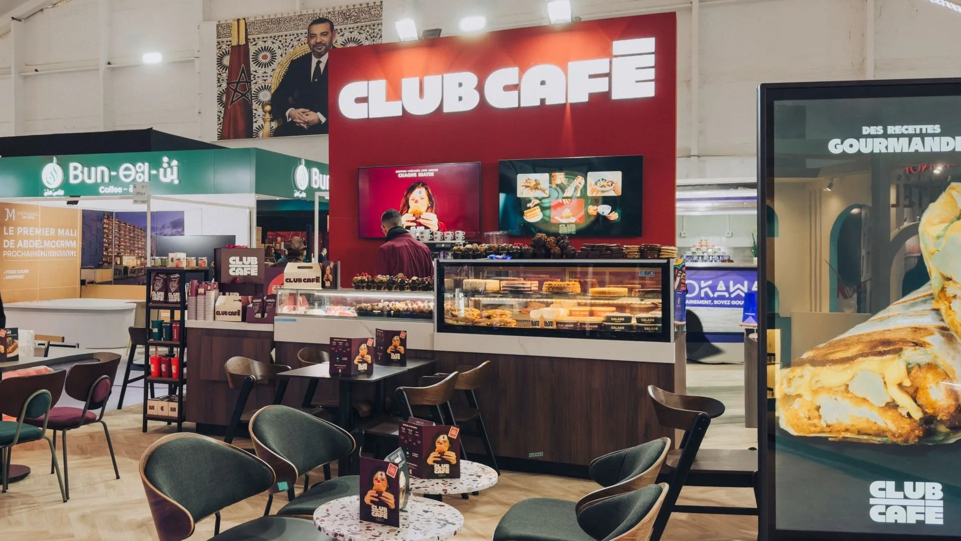Stand Club Café au Franchise Exhibition Morocco 2026 : mur de marque rouge avec enseigne lumineuse Club Café, comptoir pâtisserie, écrans et espace d’accueil